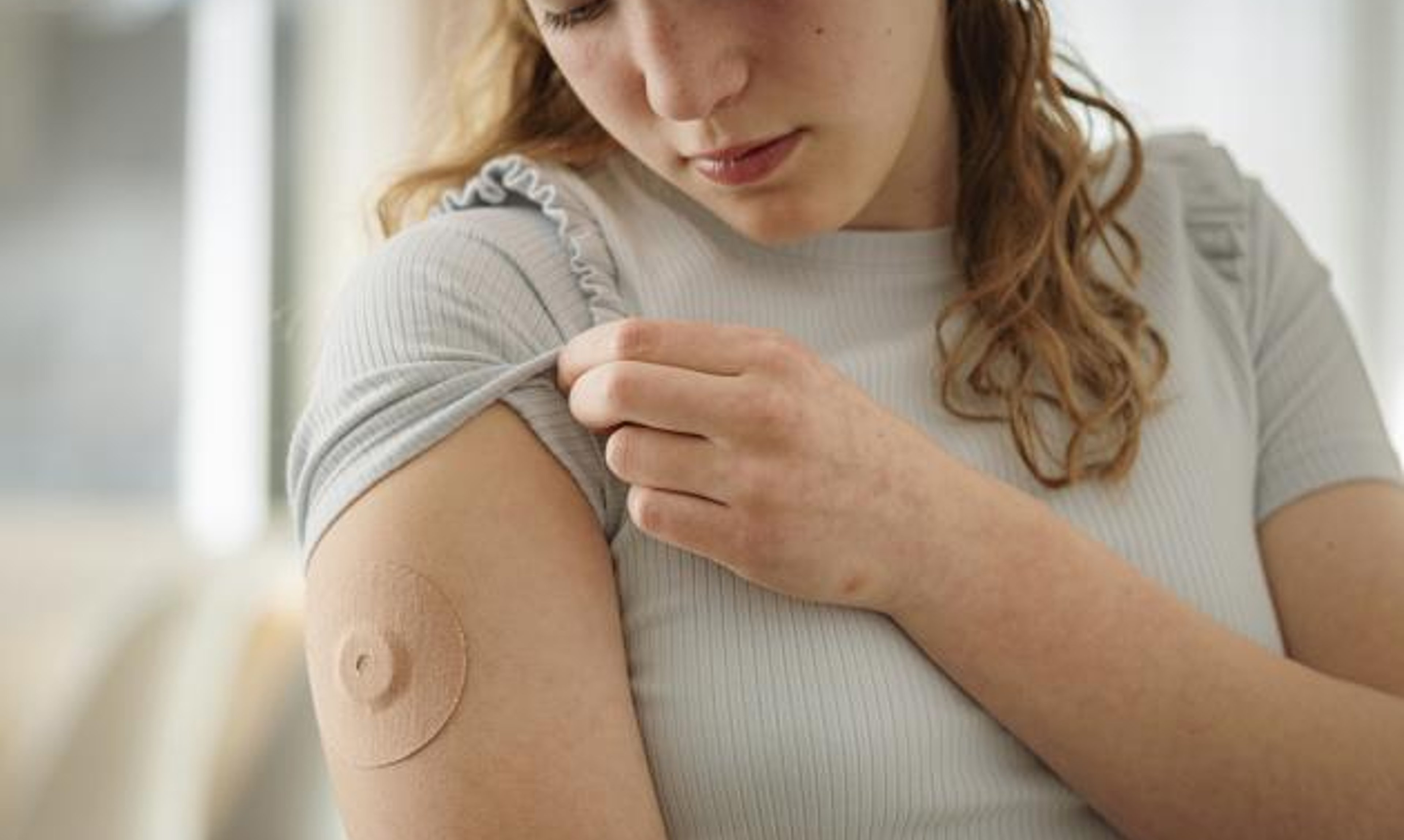A woman wearing a continuous glucose monitor looks at the fabric overlay to keep it in place.