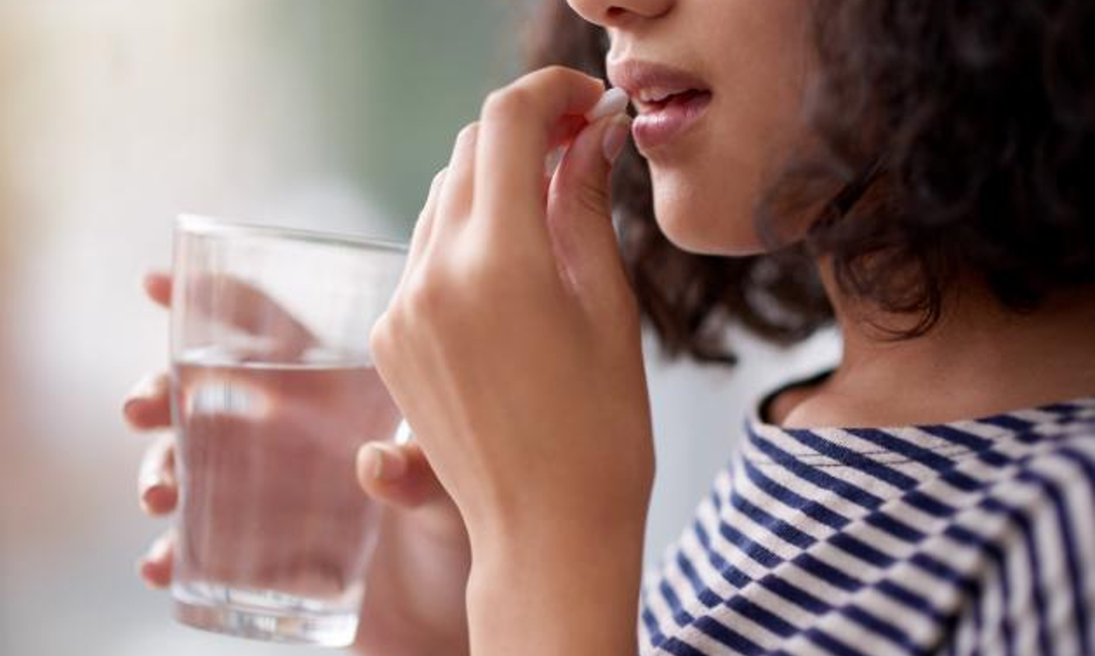 Close-up of young teenage female taking pill with a glass of water
