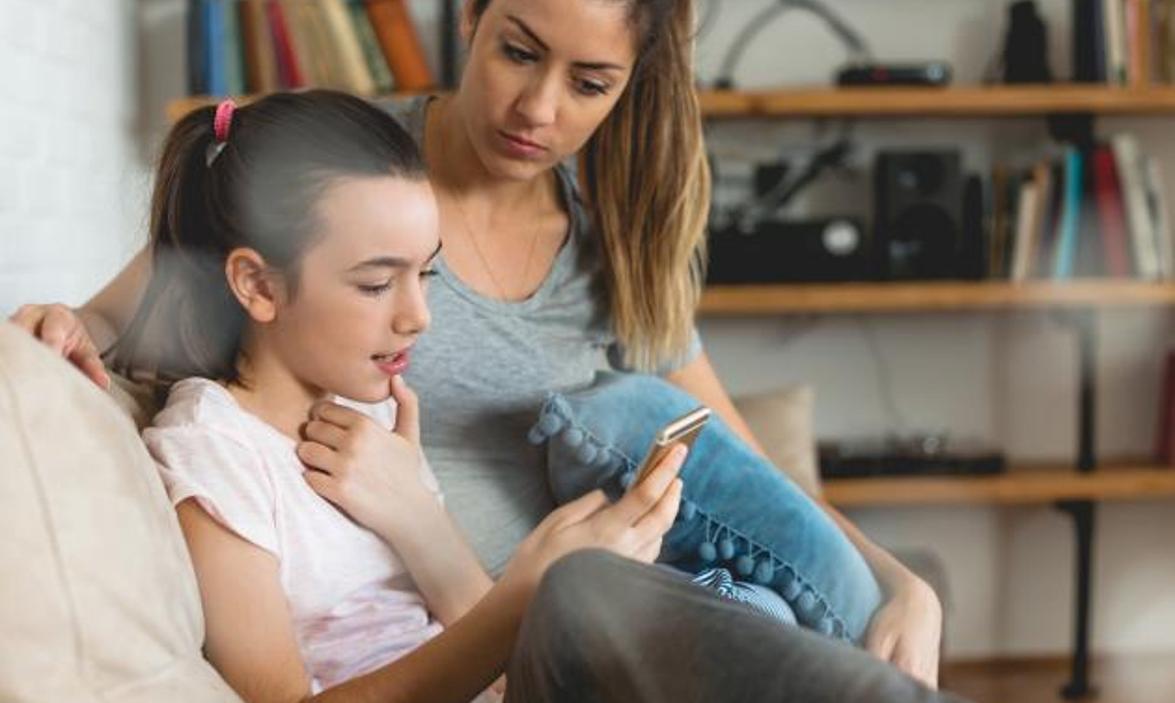 Mother and daughter look at a smartphone while sitting on a couch.