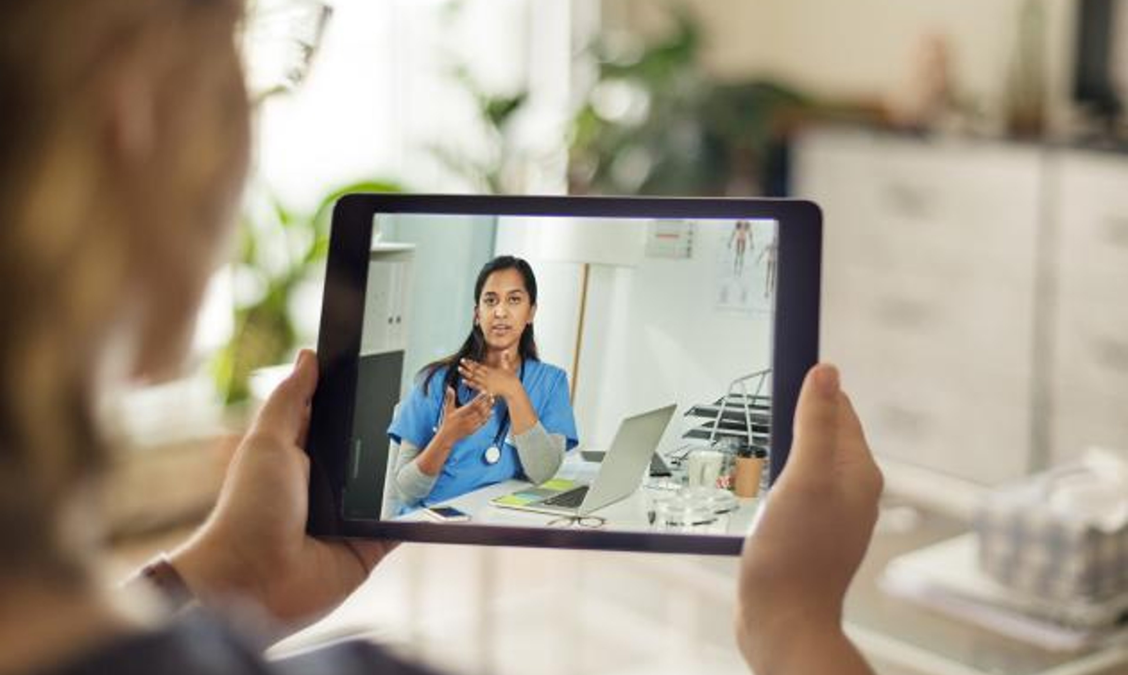 A person using a tablet computer talks to a doctor during a virtual appointment.