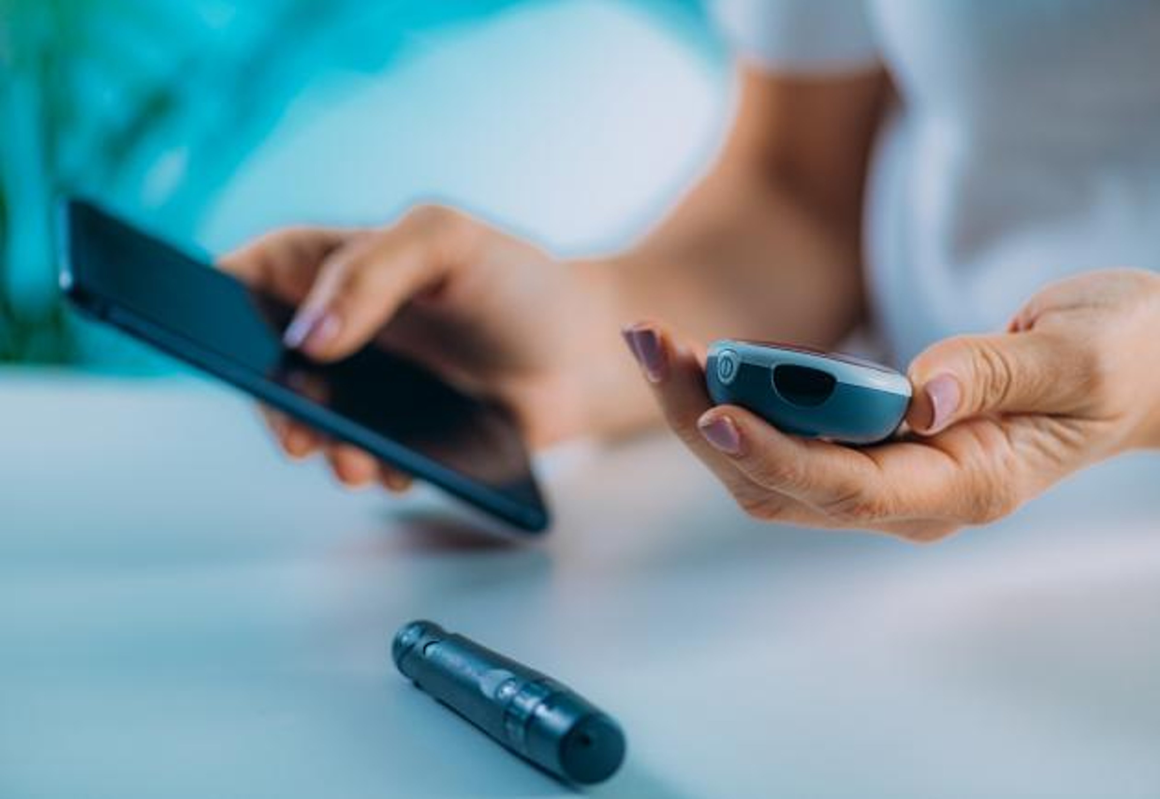 A person holding a glucometer and phone, with a lancet on a desk.