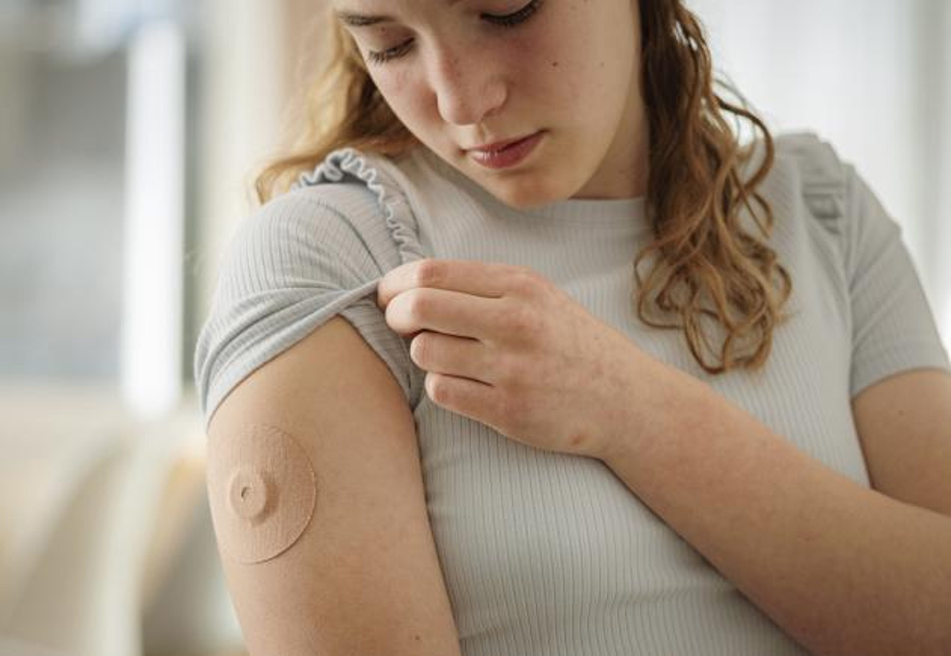 A woman wearing a continuous glucose monitor looks at the fabric overlay to keep it in place.