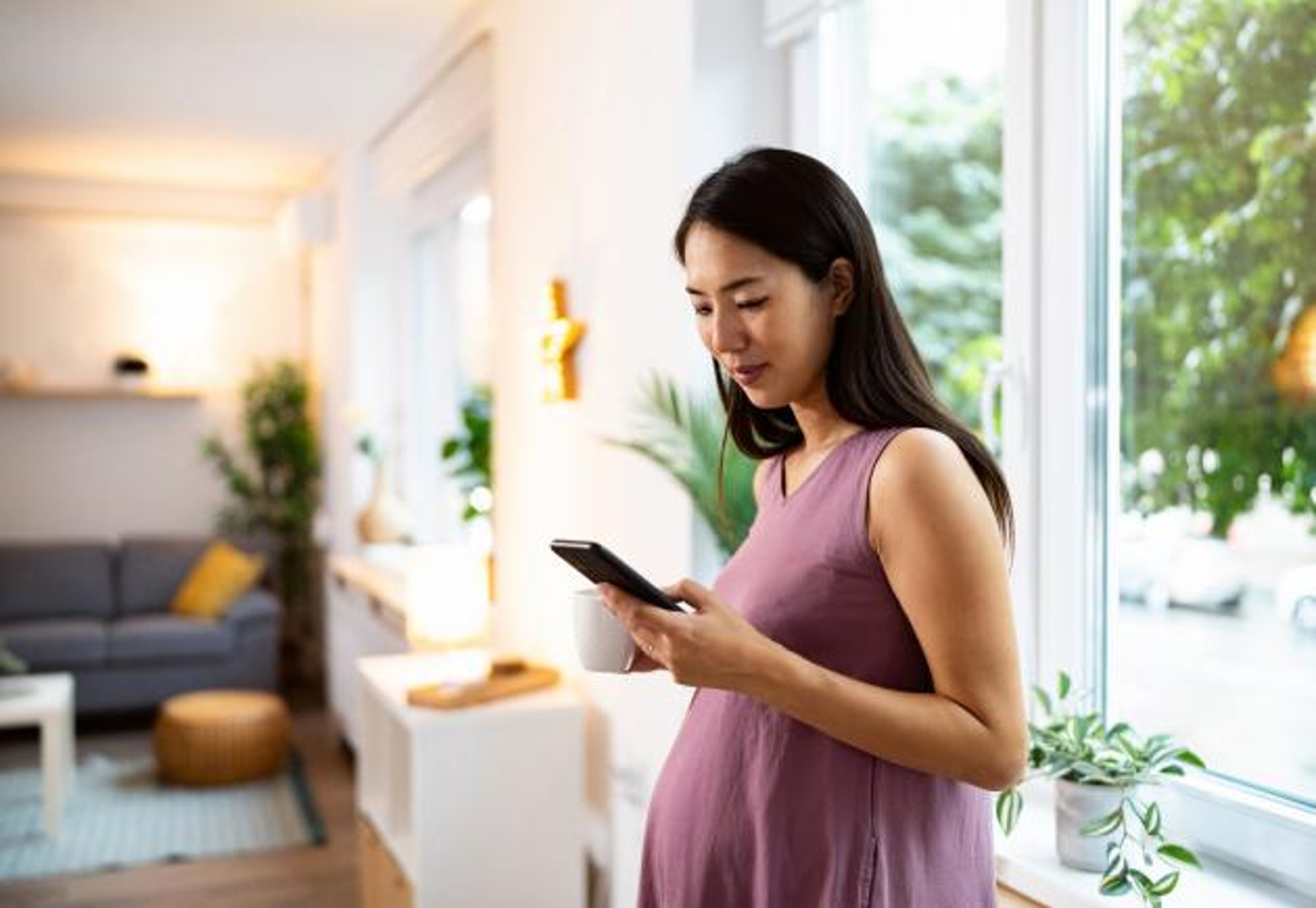 Woman who is pregnant holds a smartphone at home.