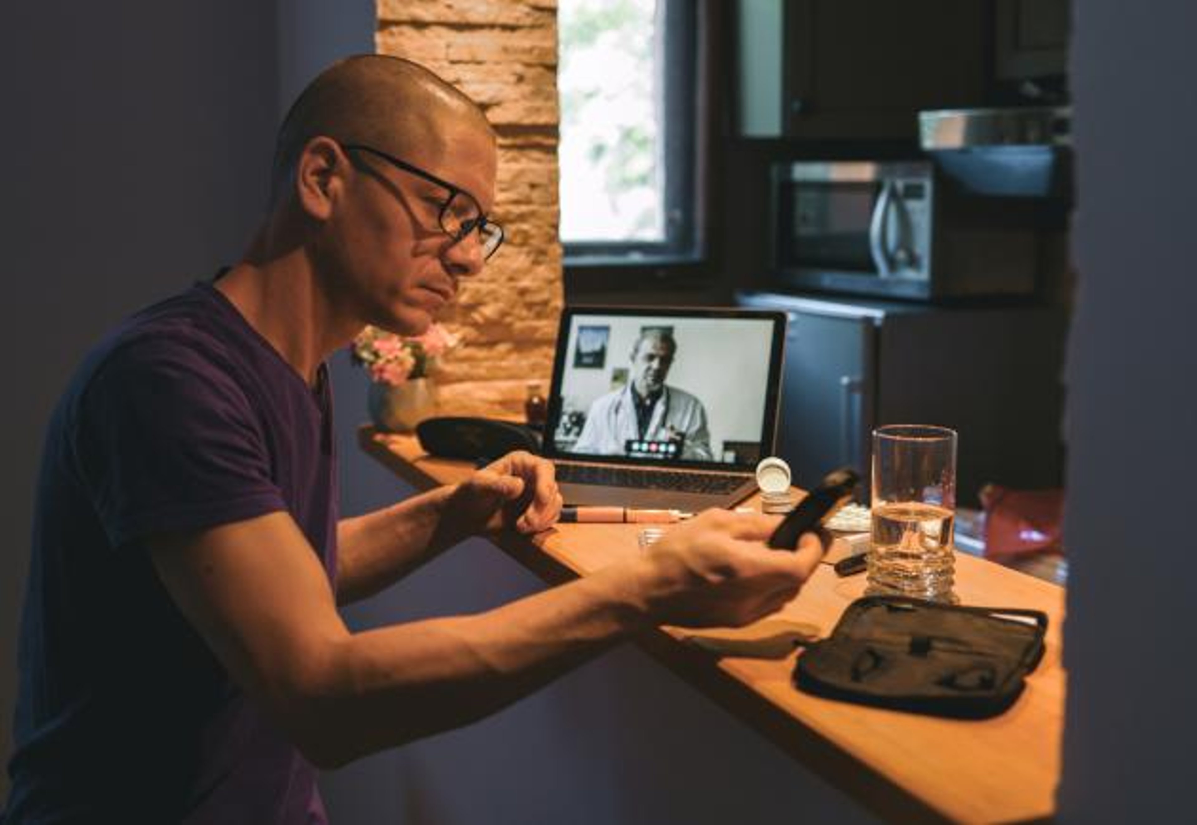 A man looks at a glucometer in his home during a telehealth visit.