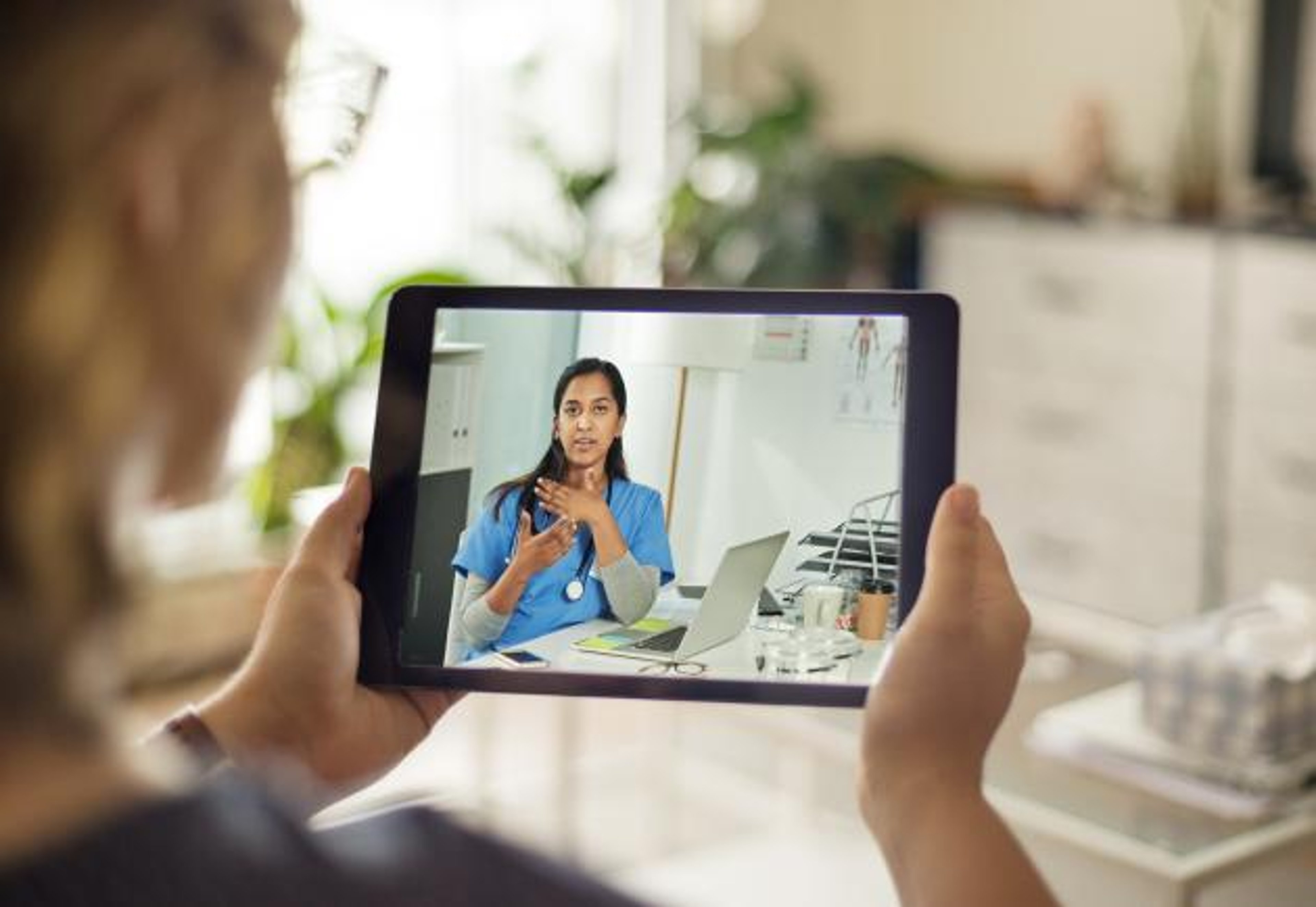A person using a tablet computer talks to a doctor during a virtual appointment.