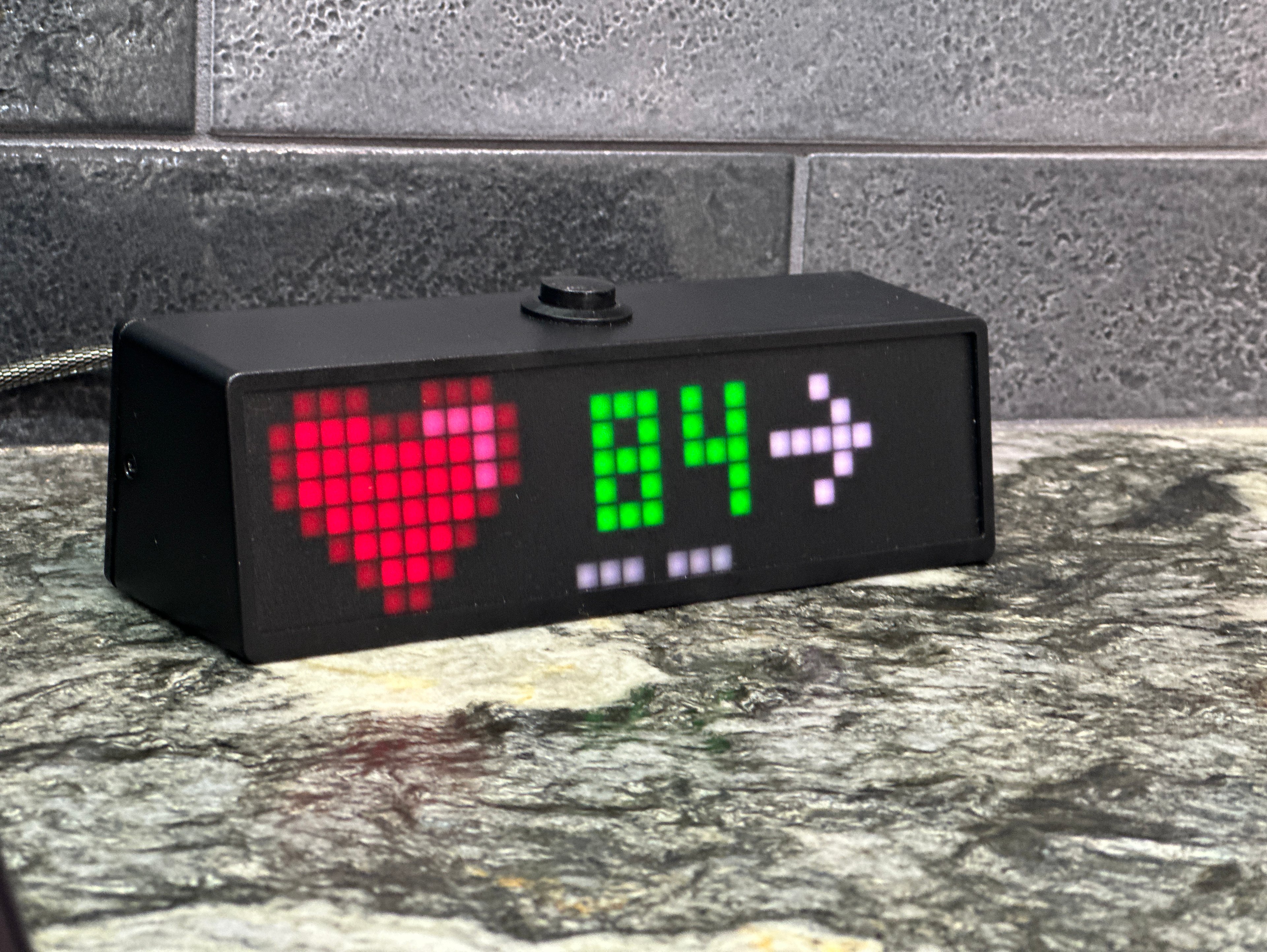 SugarPixel display sitting on a table showing an 84 mg/dL blood sugar level and a heart.