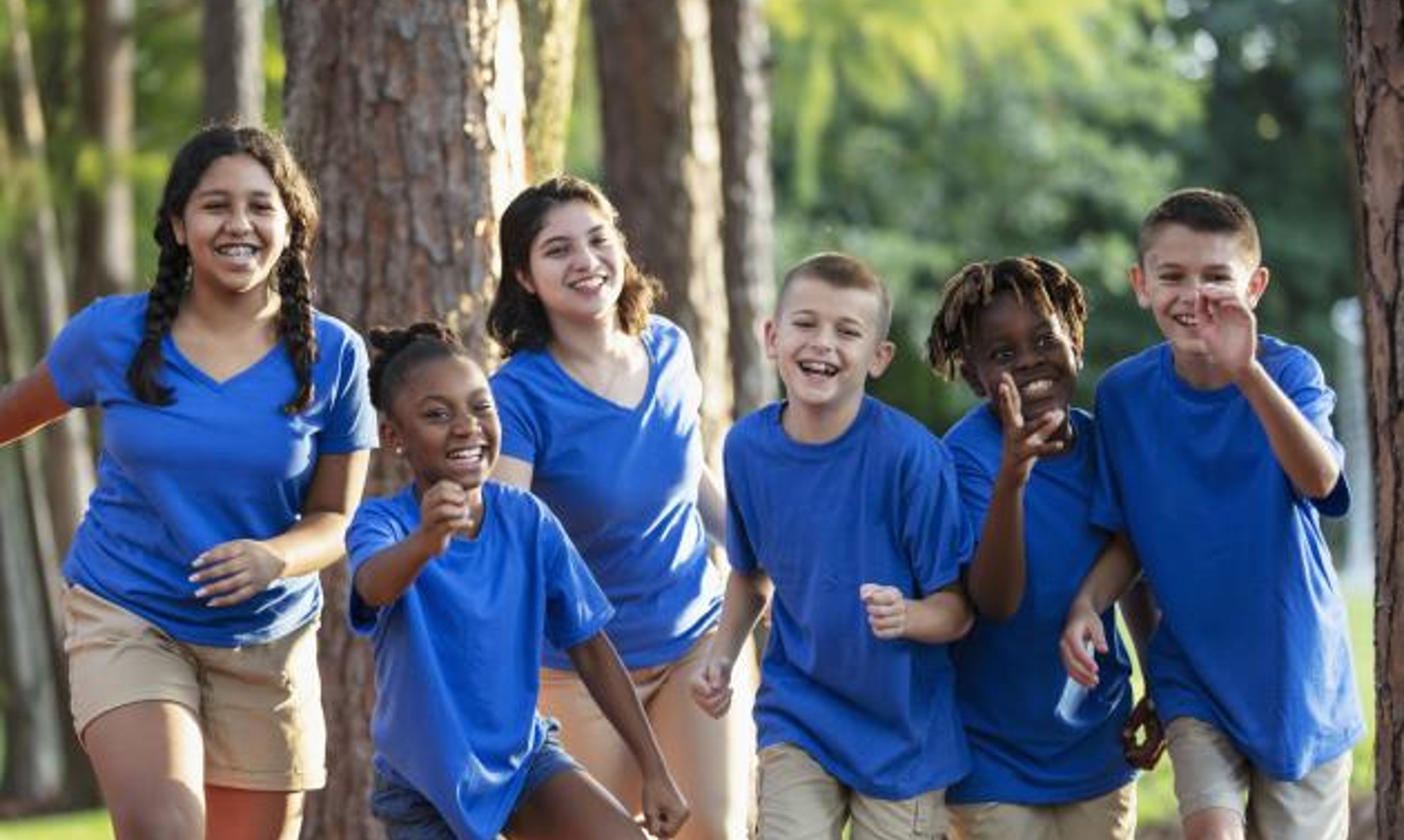 6 children running toward camera wearing camp gear with forest background