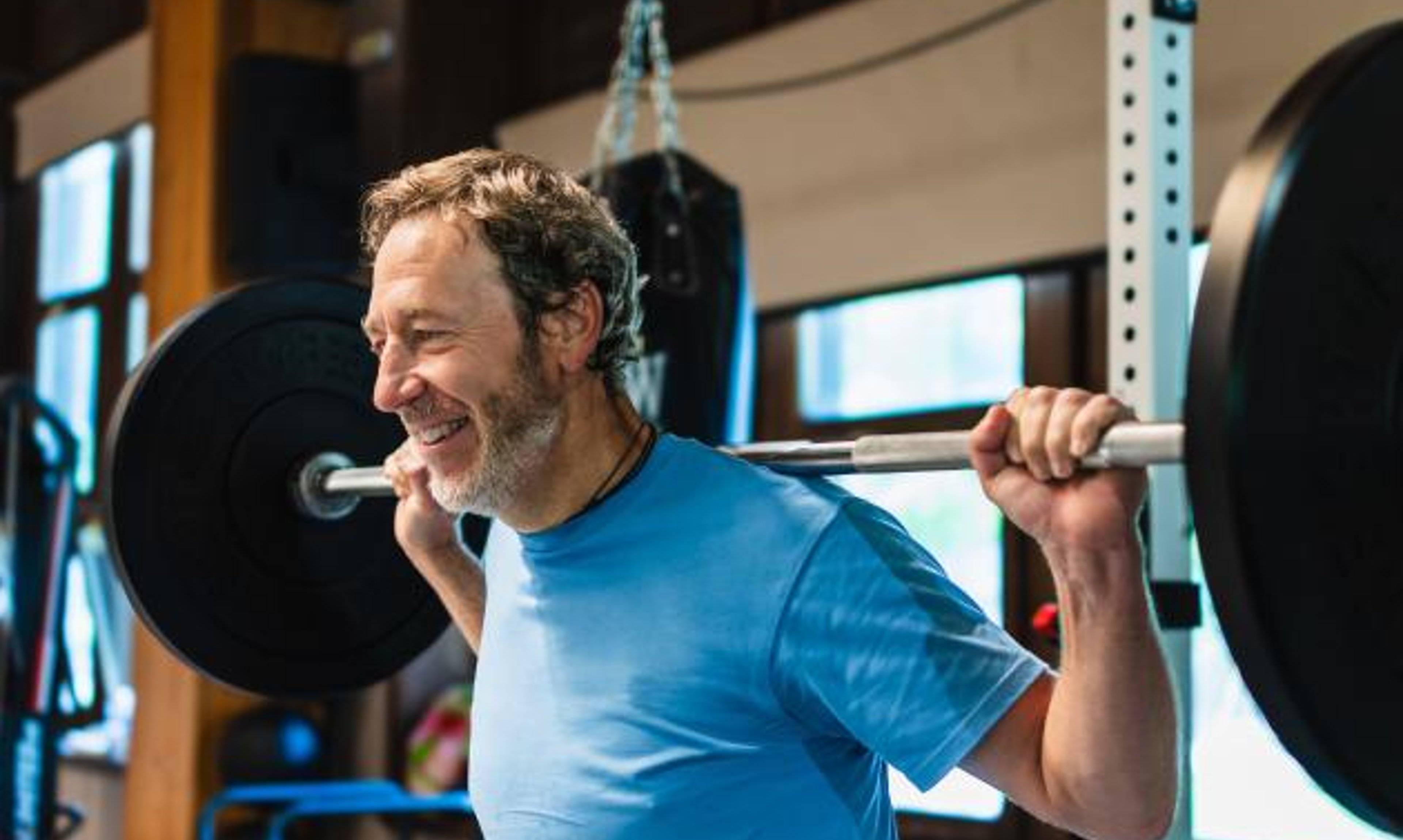 A man with a barbell on his back and a smile on his face