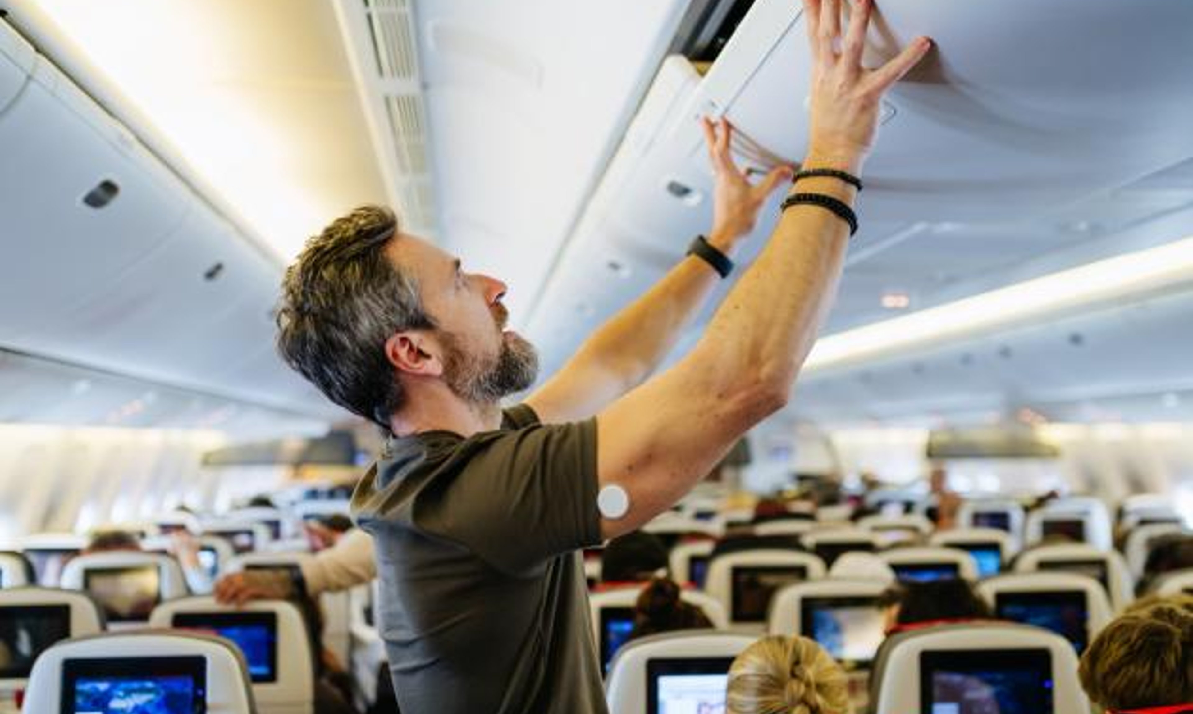 A man with a CGM closes an airplane overhead compartment
