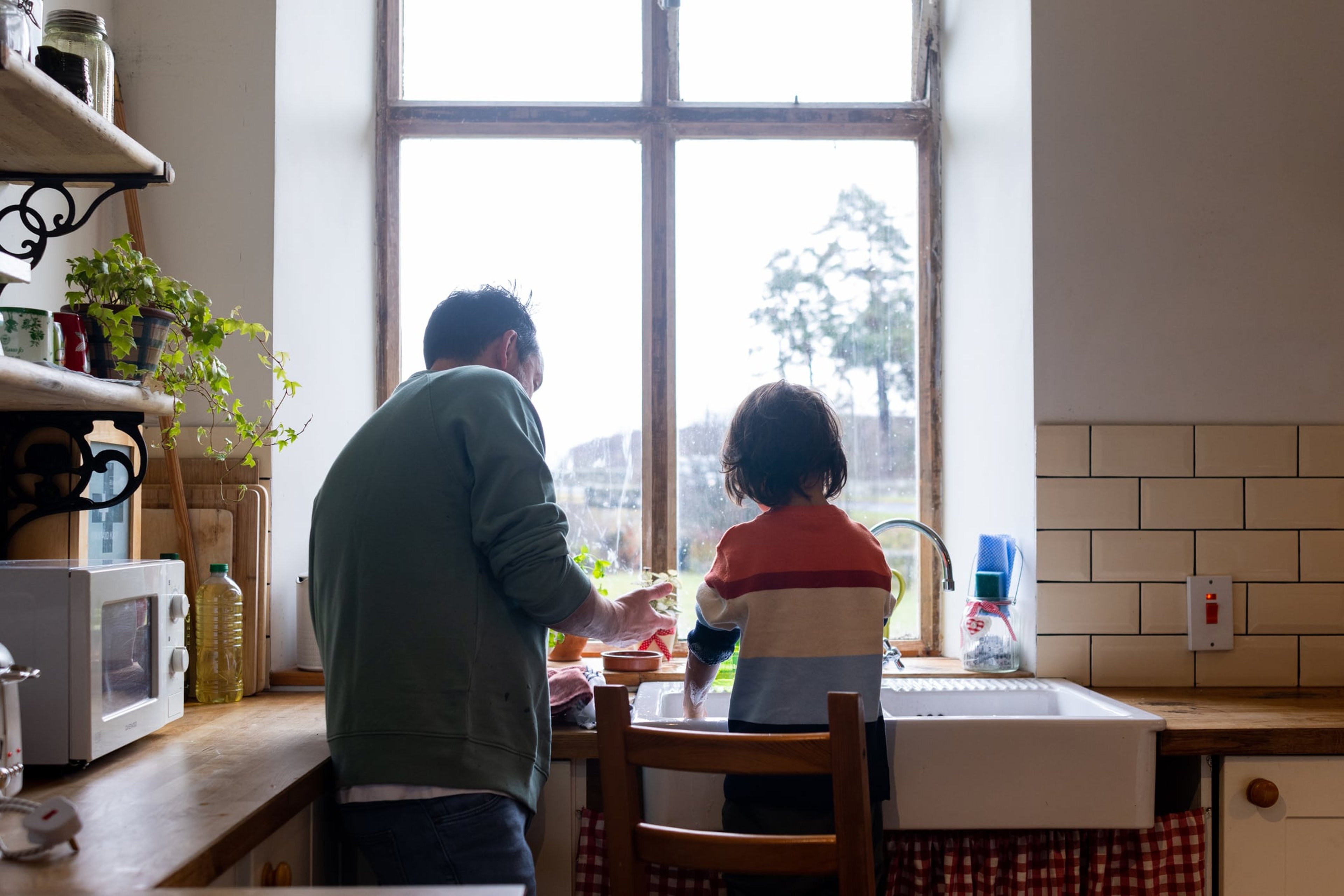 Father and child on stool wash dishes after meal