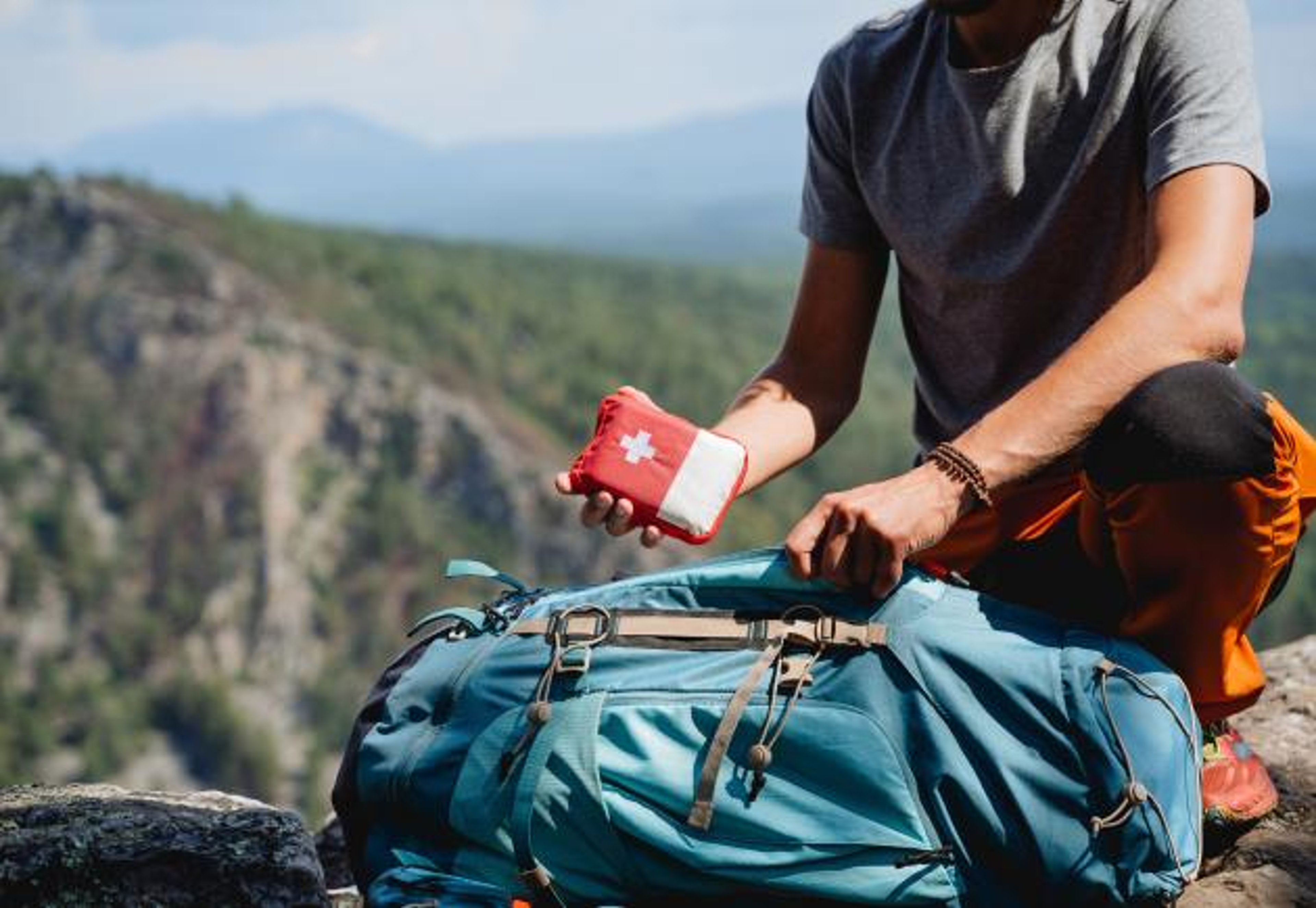 A hiker in the mountains packs a medicine kit in a backpack.