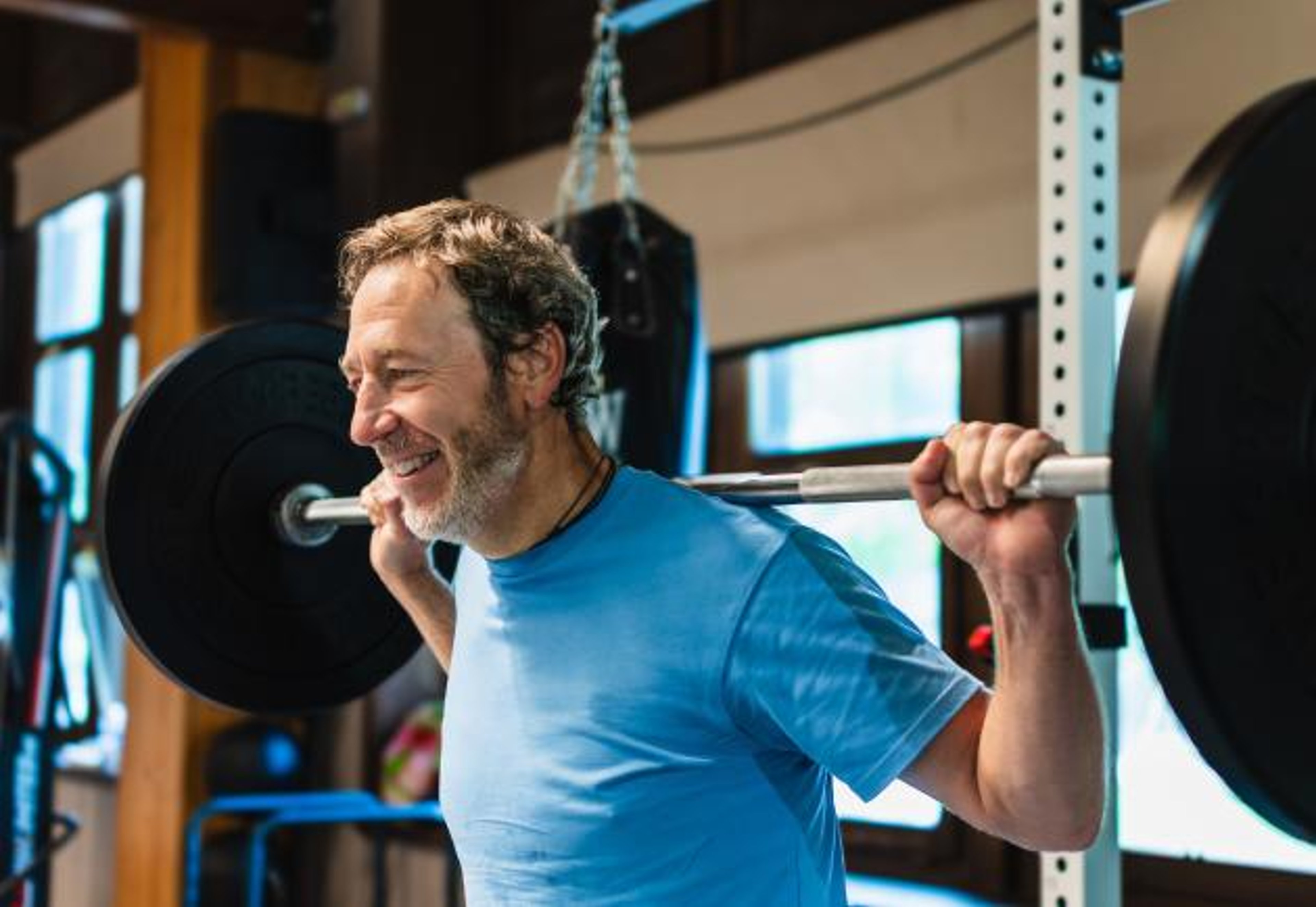 A man with a barbell on his back and a smile on his face