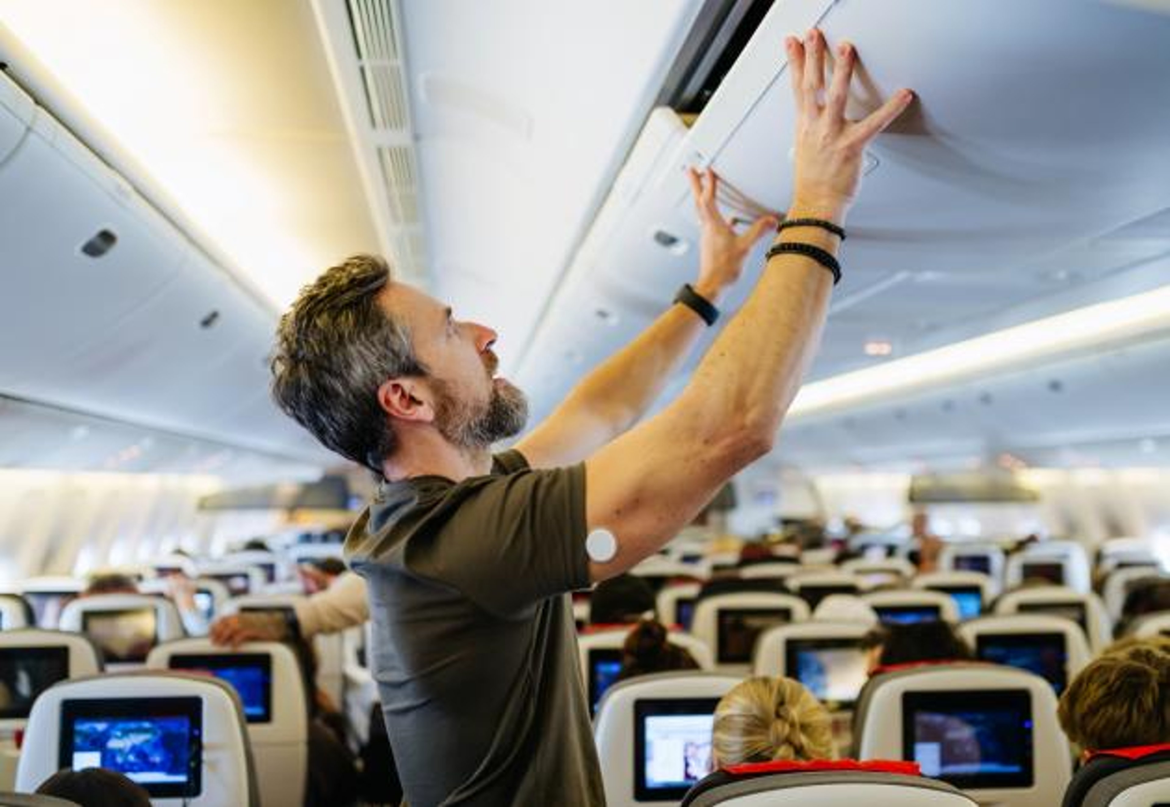 A man with a CGM closes an airplane overhead compartment
