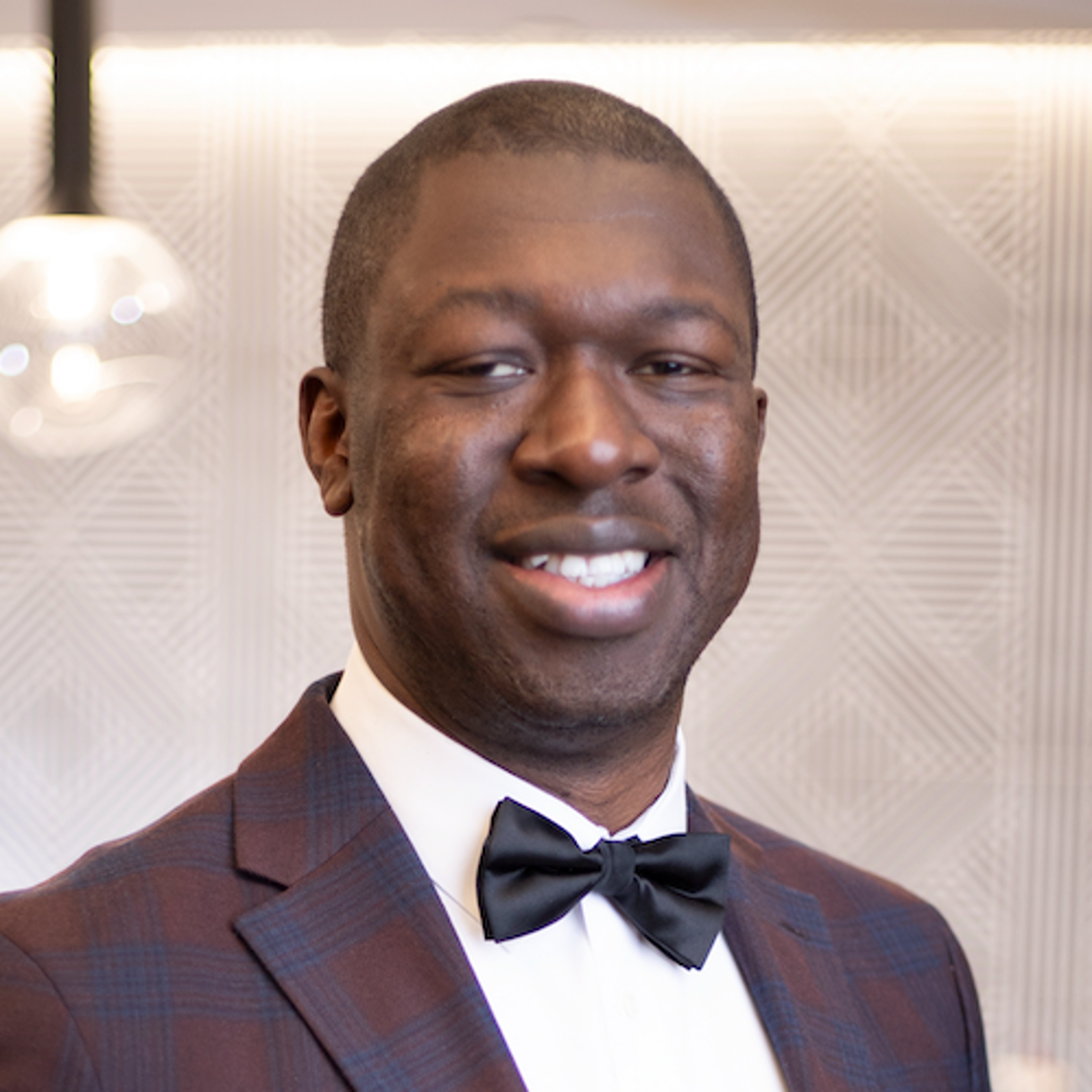 Photo of Dr. Osagie Ebekozien, a black man in a plaid jacked with bow tie
