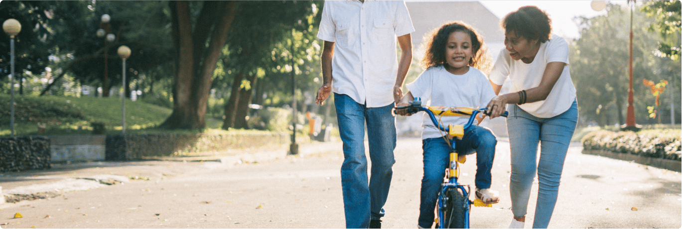 A happy father and mother, walking with their daughter whom is on a bike